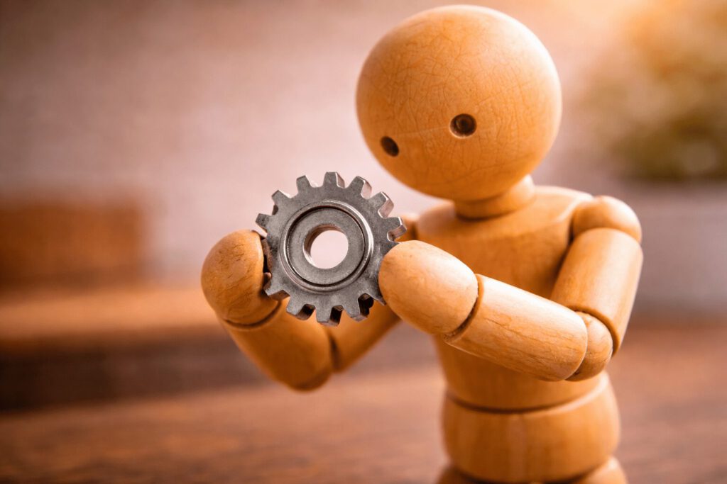 Eine Gliederpuppe betrachtet konzentriert ein Zahnrad in ihrer Hand. Symbolbild für den Karriereanker Technisch-funktionale Kompetenz, der für Expertenwissen, Fachlaufbahnen und die Liebe zum Detail steht.