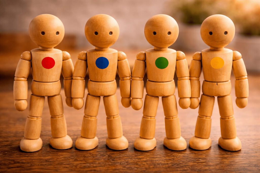 Vier Gliederpuppen mit unterschiedlich farbigen Punkten auf der Brust.