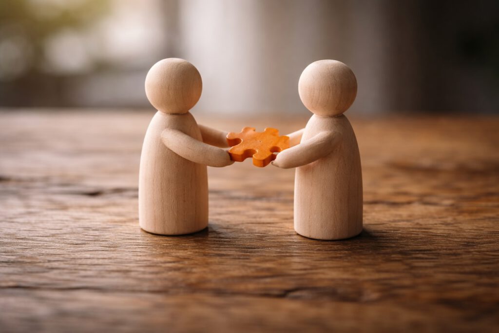Symbolbild für Feedback als Führungsinstrument: Holzfiguren im Dialog, eine Figur reicht der anderen ein Puzzleteil – Coaching Harald Braun.
