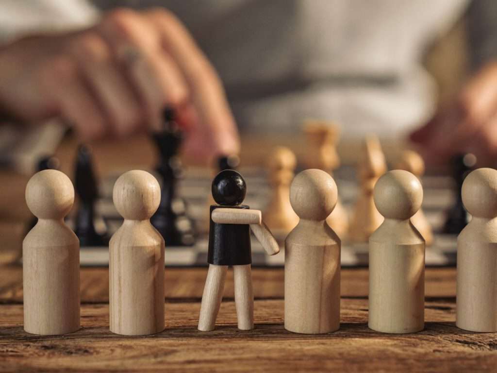 Umgang mit Low Performern visualisiert durch Holzfiguren: Eine Figur bricht provokant aus der Reihe aus – Coaching Harald Braun.